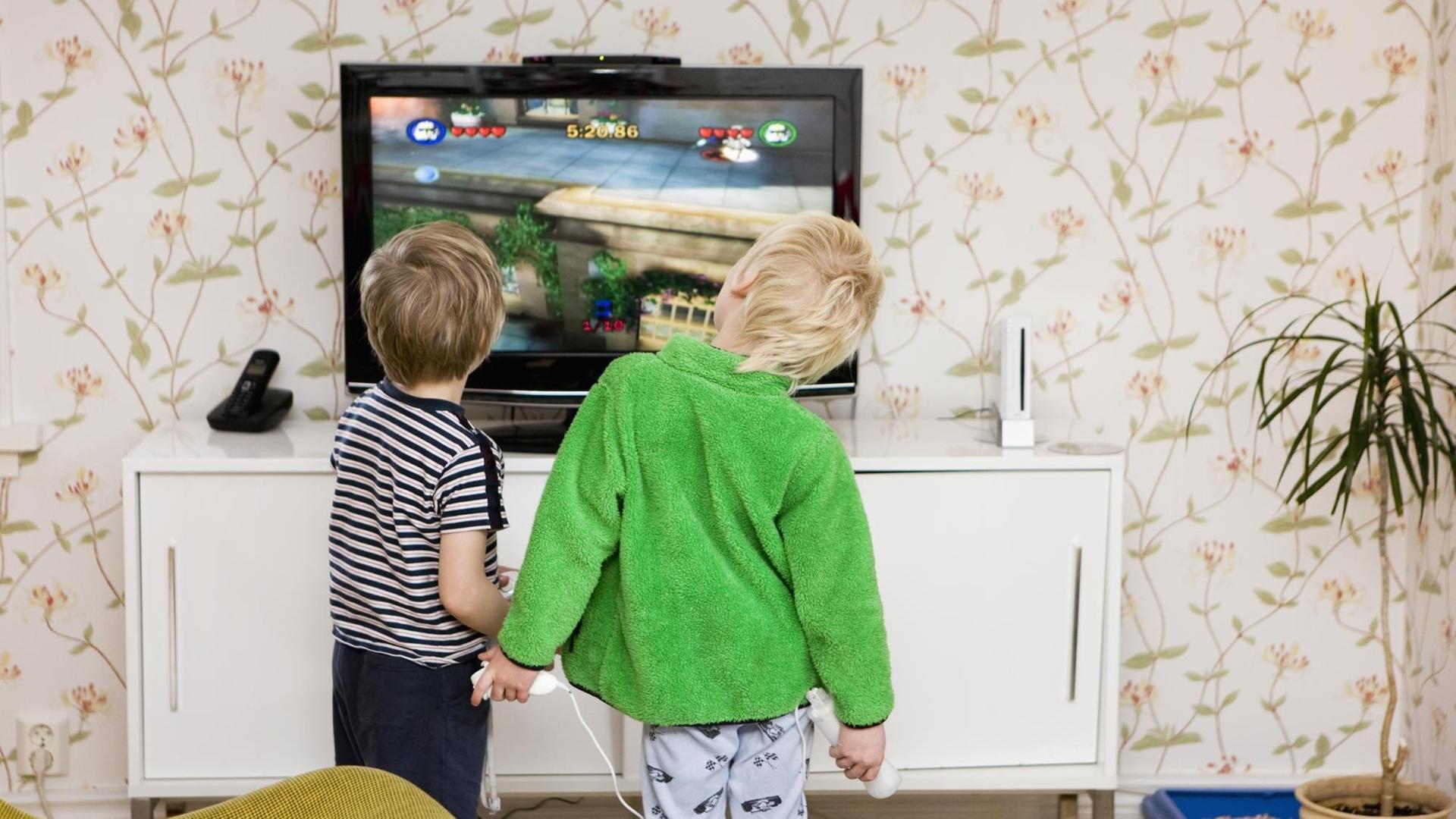 Kinder stehen vor einem Bildschirm und halten Spielekonsolen in den Händen.