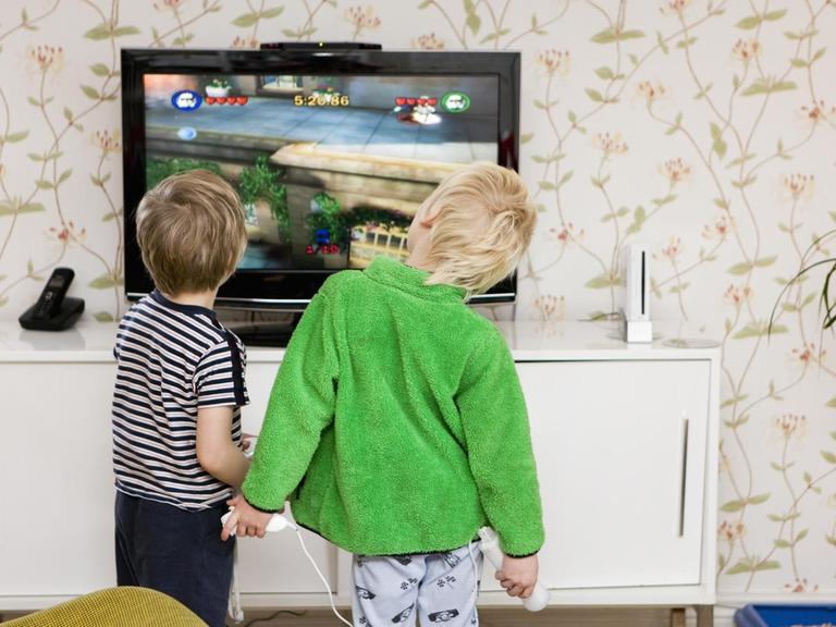 Kinder stehen vor einem Bildschirm und halten Spielekonsolen in den Händen.