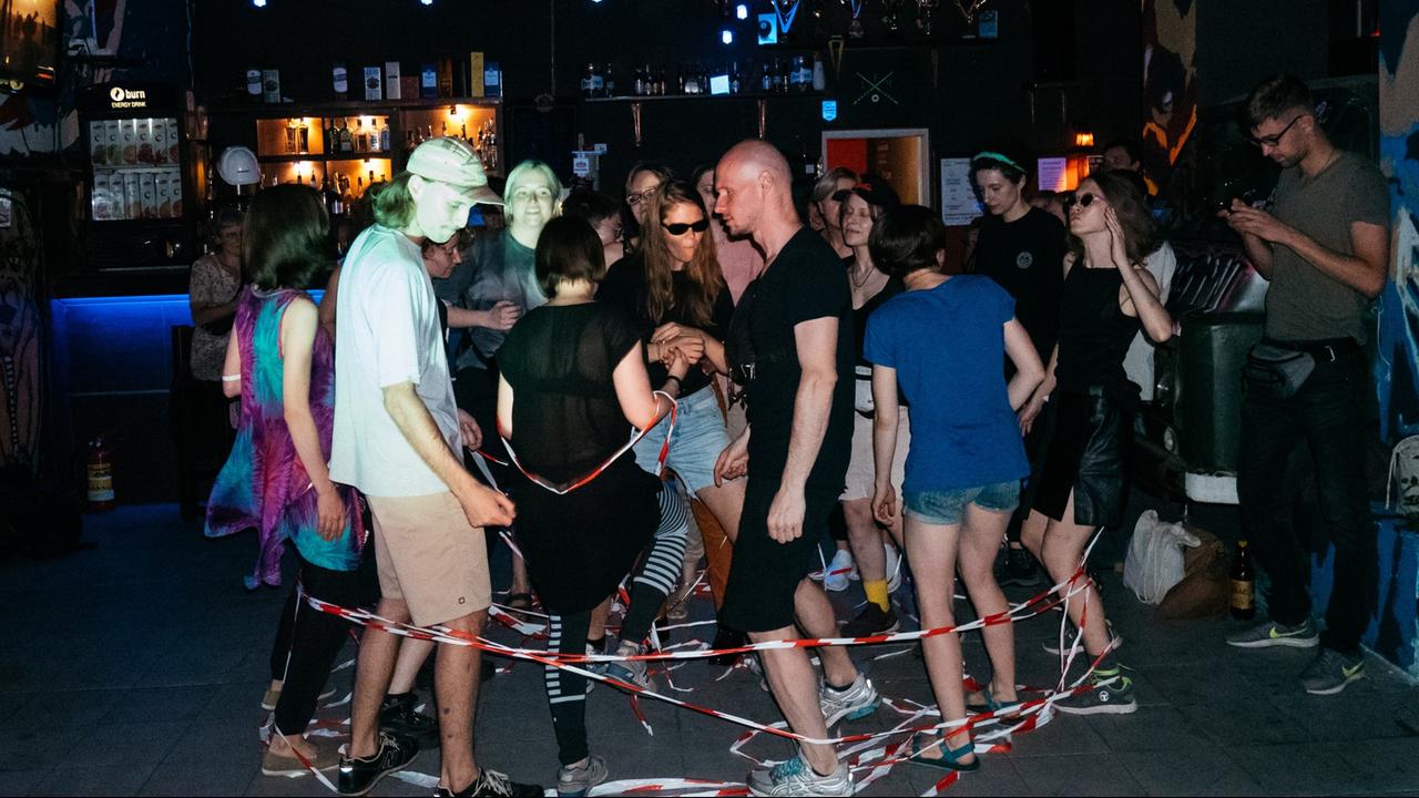 Junge Menschen tanzen in einem Technoclub, um ihre Beine windet sich rot-weißes Klebeband
