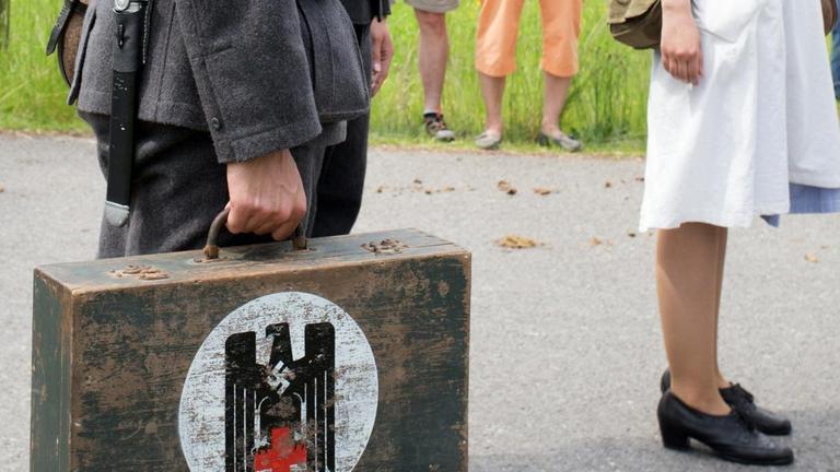 Das Bild zeigt einen Mann in der damaligen Rot-Kreuz-Uniform mit einem Koffer in der Hand, auf dem sowohl das Rote Kreuz als auch das Hakenkreuz abgebildet sind.