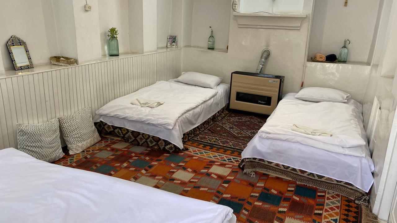 Ein Zimmer mit zwei weiß bezogene Betten auf einem bunten Teppich und einem Ofen dazwischen.