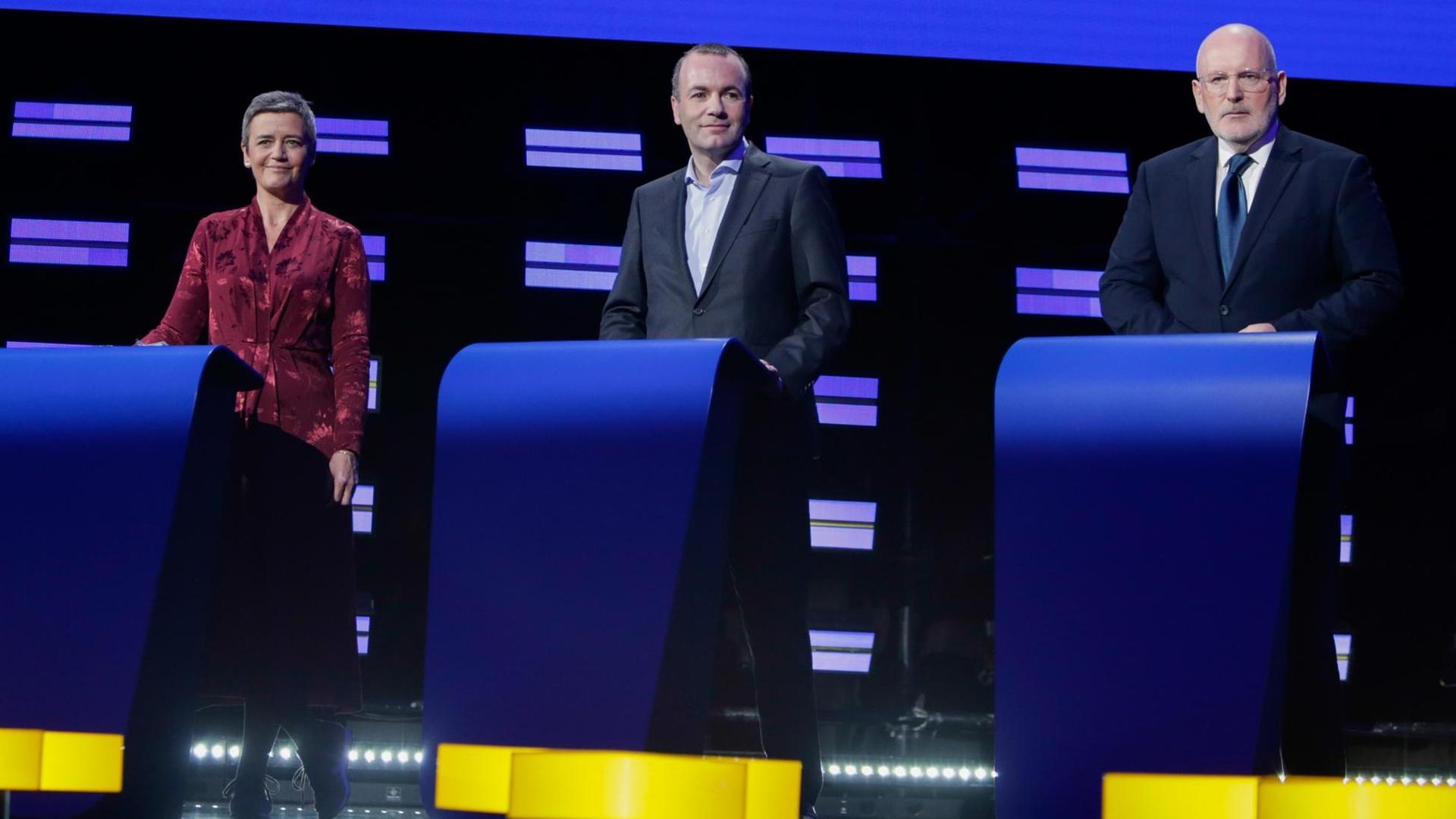 Margrethe Vestager, Manfred Weber und Frans Timmermans stehen nebeneinander jeweils hinter einem Pult auf einer Bühne