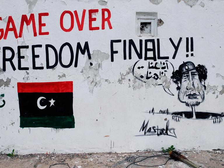 Bemalte Mauer in der libyschen Hauptstadt Tripolis: Zu sehen ist eine libysche Flagge in den Nationalfarben, die Aufschrift "Game over - Freedom finally" und ein Gaddafi, der aus einem Abfluss schaut und "hier bin ich, hier bin ich" ruft.