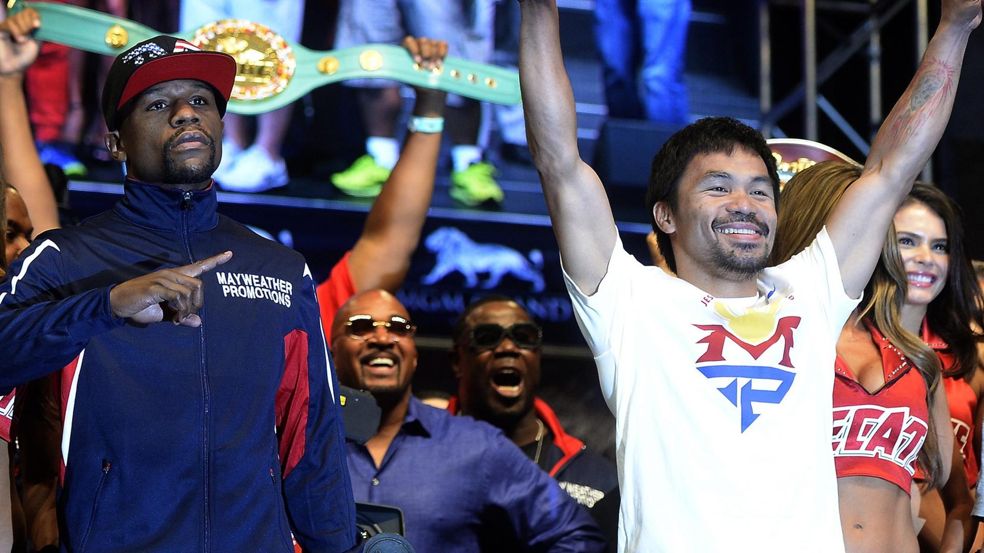 Der schwarze US-Boxer Floyd Mayweather und der Philippiner Manny Pacquiao jubeln mit Siegesgesten von einer Bühne ins Publikum.