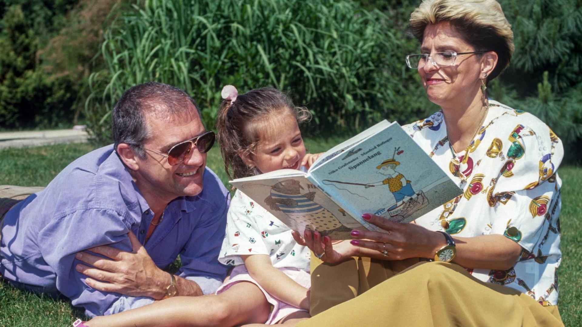 Eine Mutter liest in den 90er-Jahren ihrer Familie vor, sie sitzen auf der Wiese.