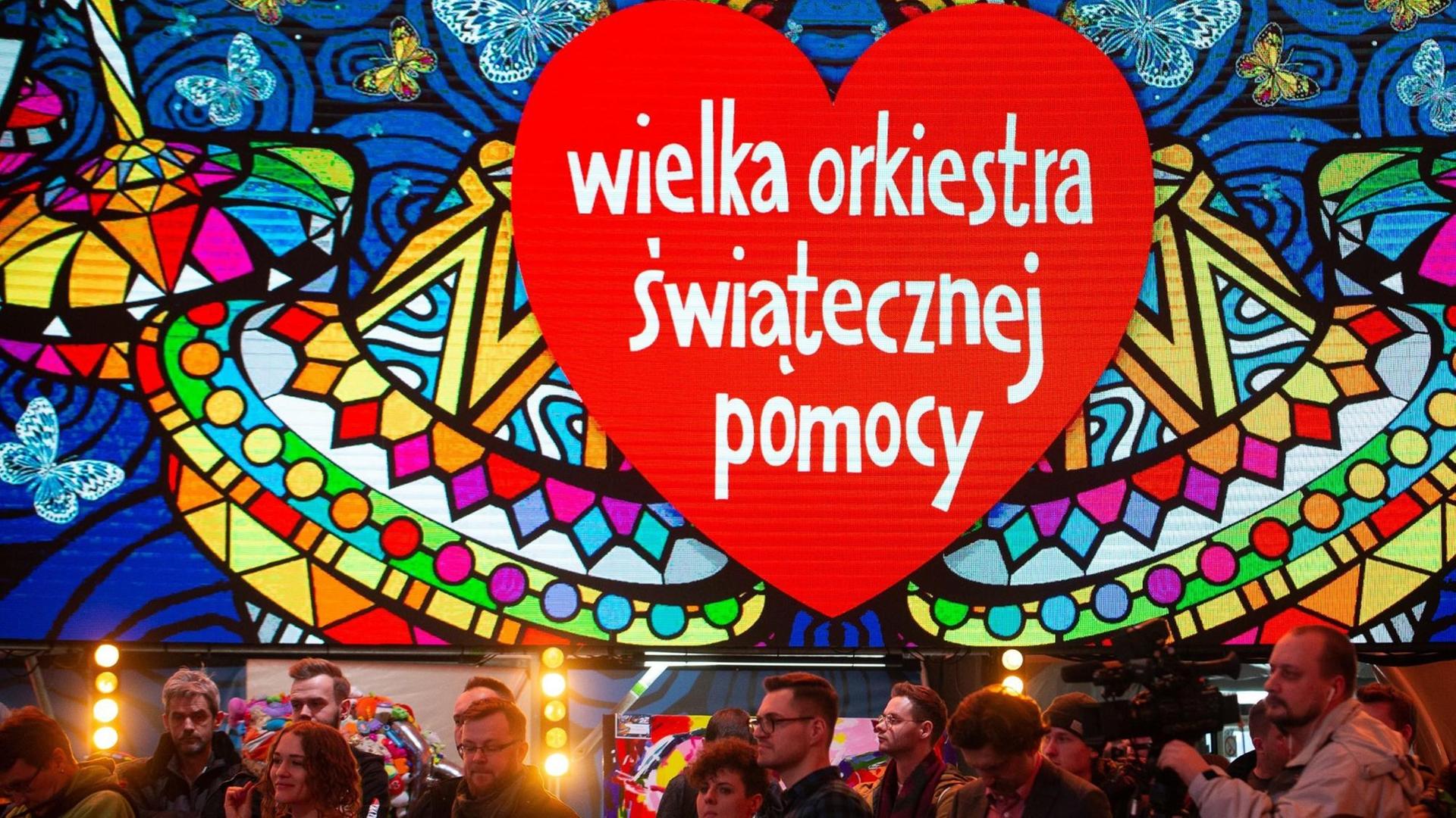 Das Logo der polnischen Benefizveranstaltung "Wielka Orkiestra Swiatecznej Pomocy" ("Großes Orchester der Weihnachtshilfe") hängt in Übergröße über Fotografen und Kamerateams in Warschau