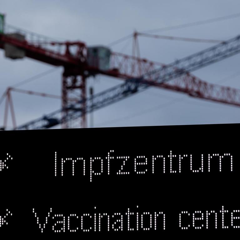 Kräne sind auf einer Baustelle hinter einer Hinweistafel auf den Weg zum Impfzentrum zu sehen. Die Infektionszahlen steigen, gleichzeitig fallen geplante Impfungen mit dem Impfstoff Astrazeneca aus.