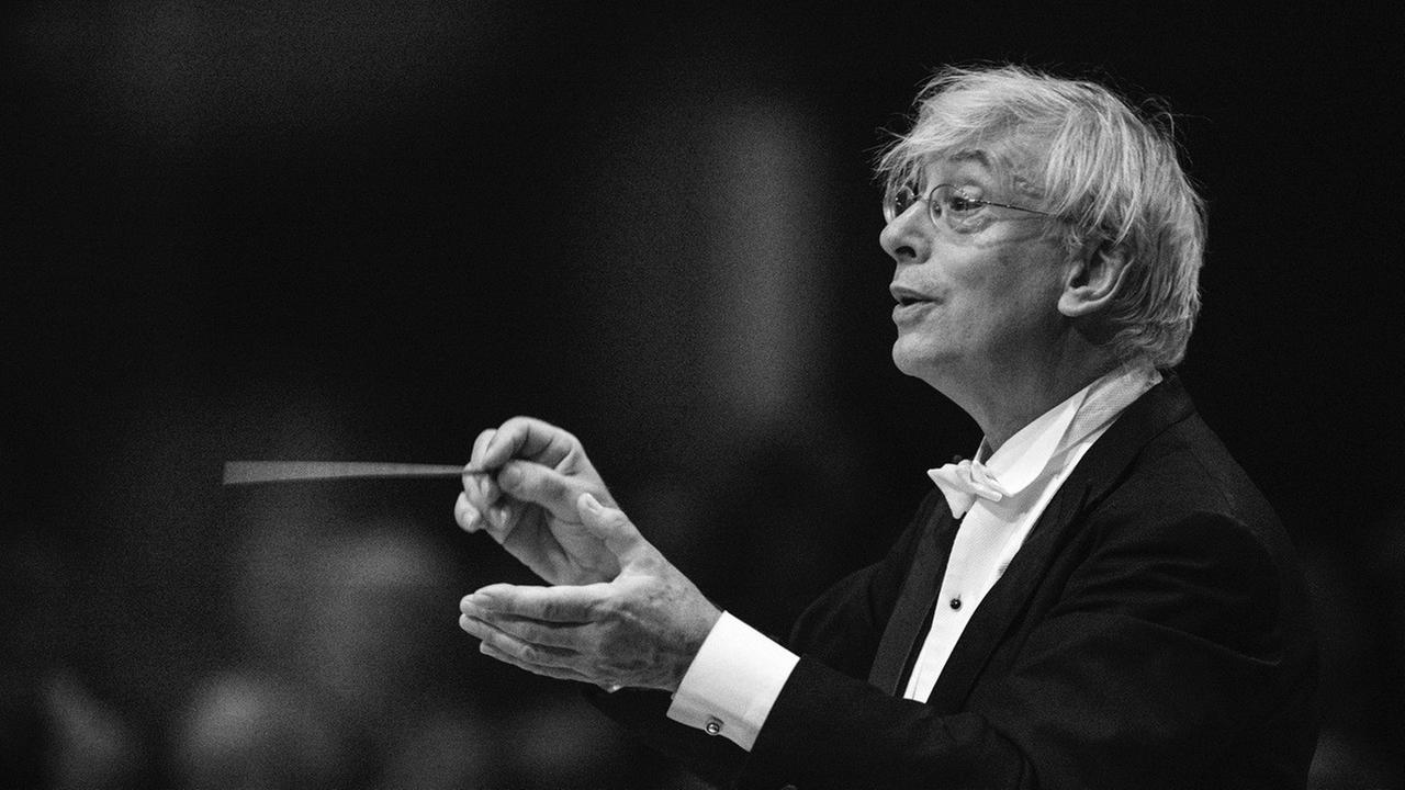 Der Dirigent Mario Venzago hält einen Taktstock in der Hand und blickt zum Orchester.