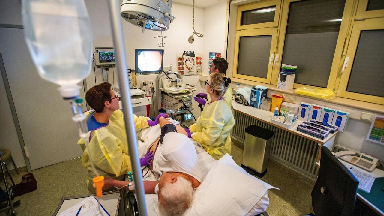 Untersuchung des Magen-Darmtraktes. Ein älterer Mann bei einer Endoskopie liegt seitlich auf dem Operationstisch. Ein Arzt bedient das Endoskop, schaut auf den Monitor und betrachtet die Dickdarmschleimhaut. 