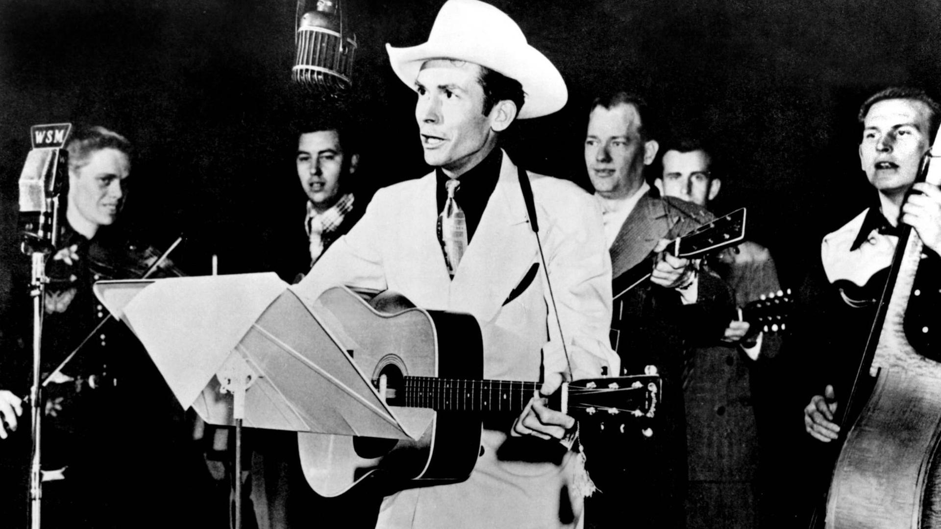 Der Musiker Hank Williams mit Gitarre und Cowboyhut bei einem Auftritt.