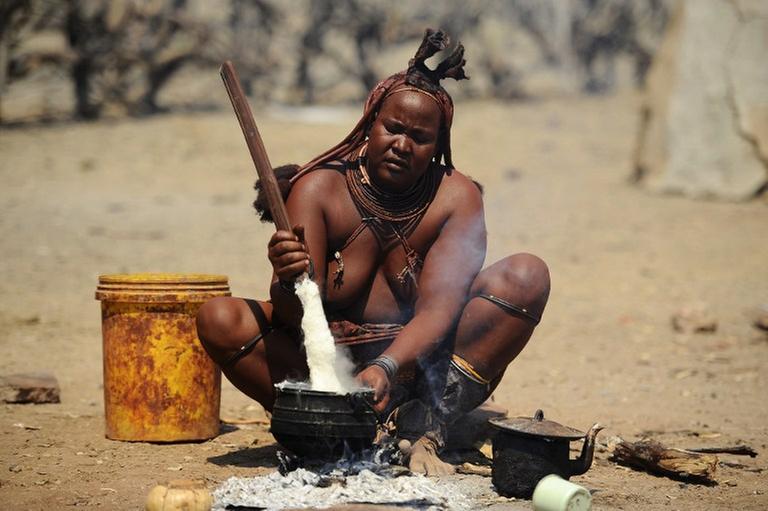 Eine Himba-Frau bereitet Essen am Feuer. 