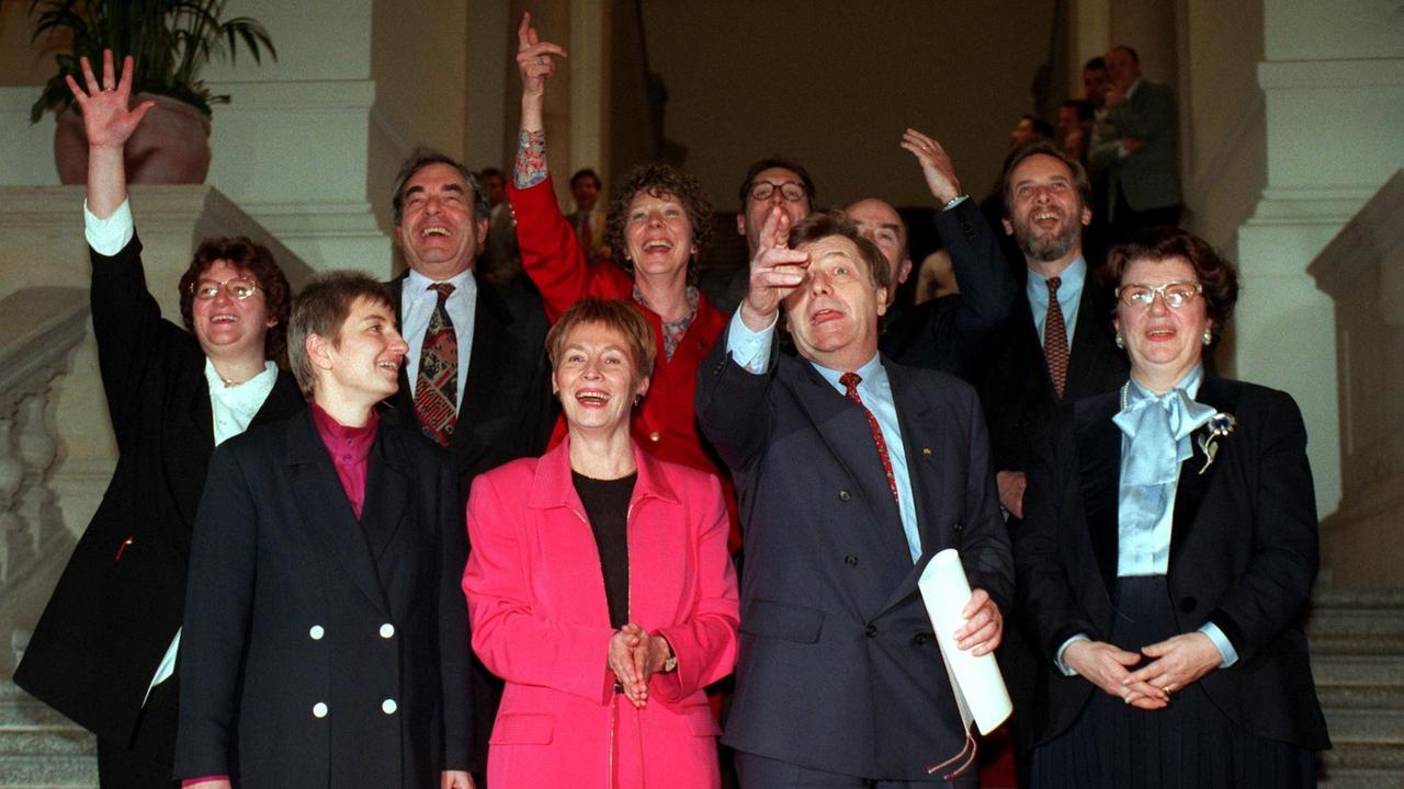 Zehn Menschen stehen auf einer Treppe und reißen vor Freude die Hände in die Luft. Es sind die Mitglieder der Berliner Regierung von 1996. 