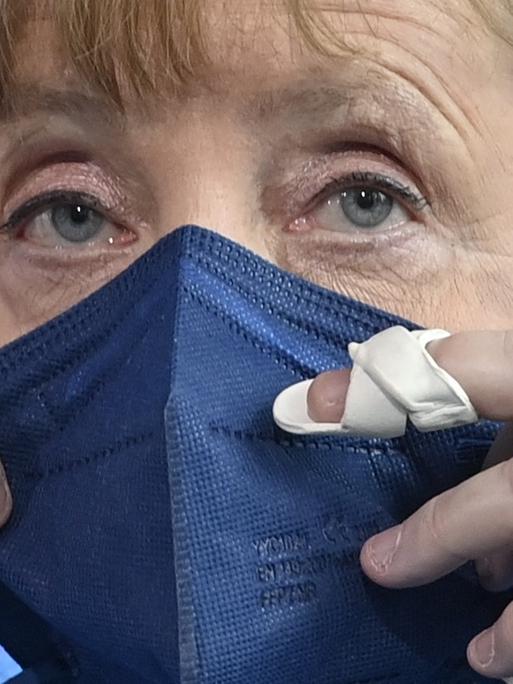 Bundeskanzlerin Angela Merkel setzt ihren Mundnasenschutz auf.