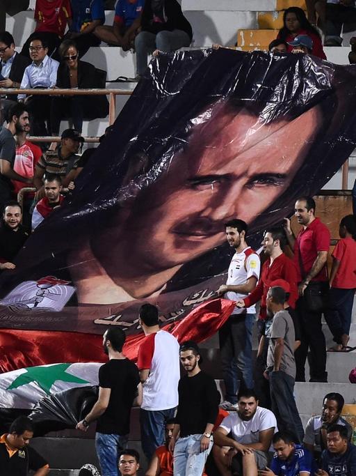 Syrische Fußballfans zeigen ein Porträt des syrischen Präsidenten Bashar al-Assad während des Qualifikationsfußballspiels der Fußball-Weltmeisterschaft 2018 zwischen Südkorea und Syrien (Archivbild 2016)