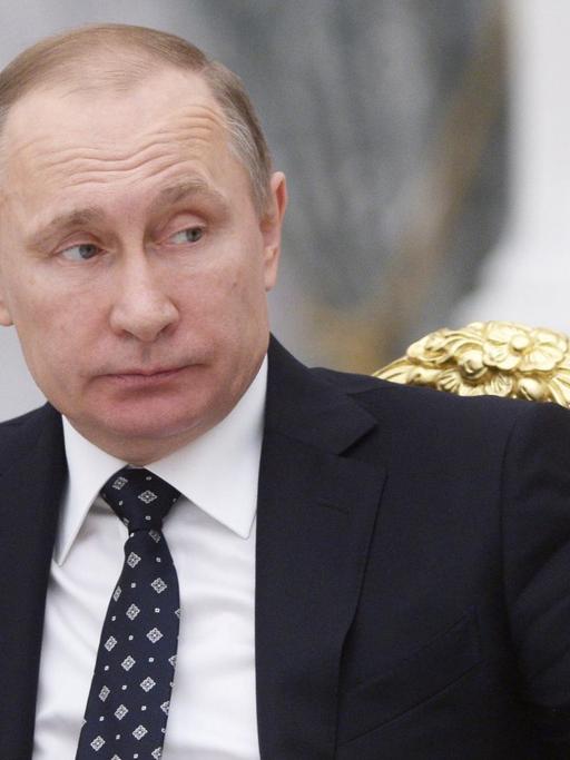 Russlands Präsident Putin sitzt im Kreml vor einem Mikrofon und blickt zur Seite