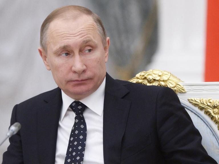 Russlands Präsident Putin sitzt im Kreml vor einem Mikrofon und blickt zur Seite