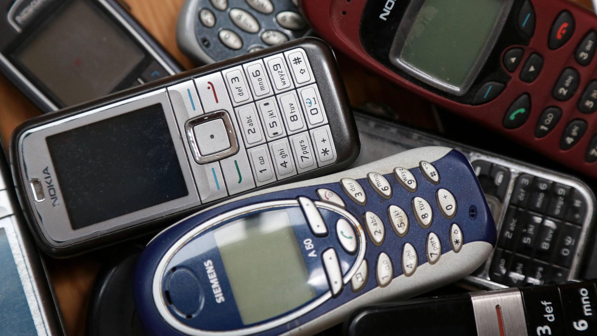 Mehrere ausgediente Mobiltelefone liegen auf einem Tisch.