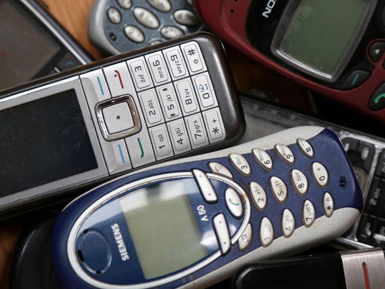 Mehrere ausgediente Mobiltelefone liegen auf einem Tisch.