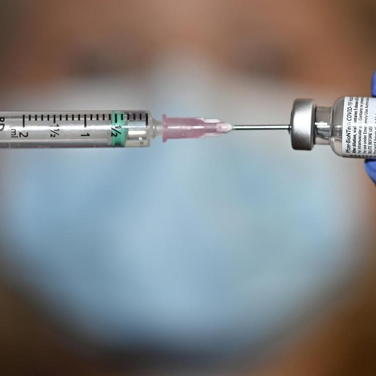 Zwei blaue Gummihandschuhe halten eine Spritze mit Coronaimpfstoff 