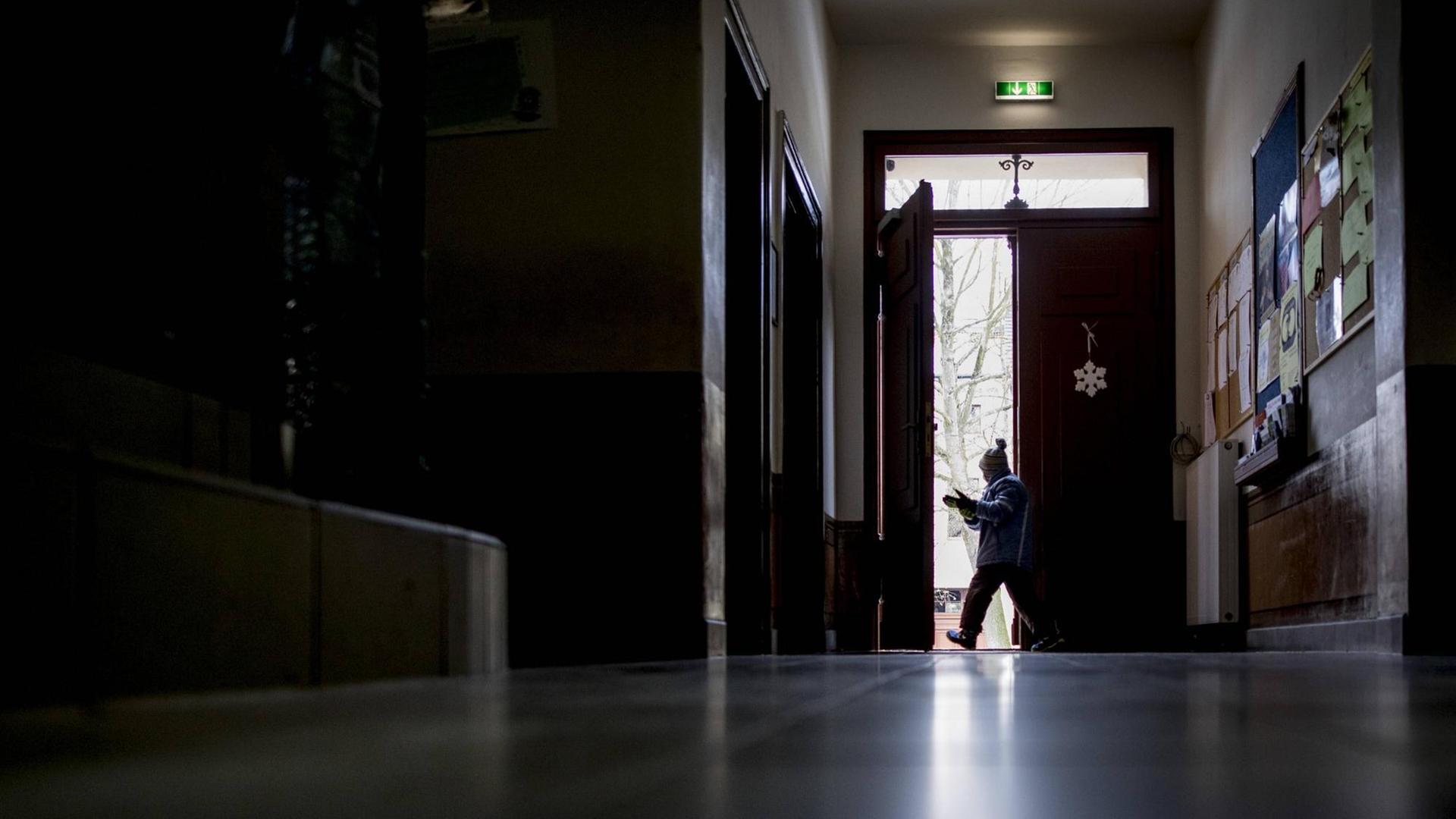 Blick durch den Gang einer Schule. Ein Schüler verlässt das Gebäude durch eine Tür am Ende des Gangs