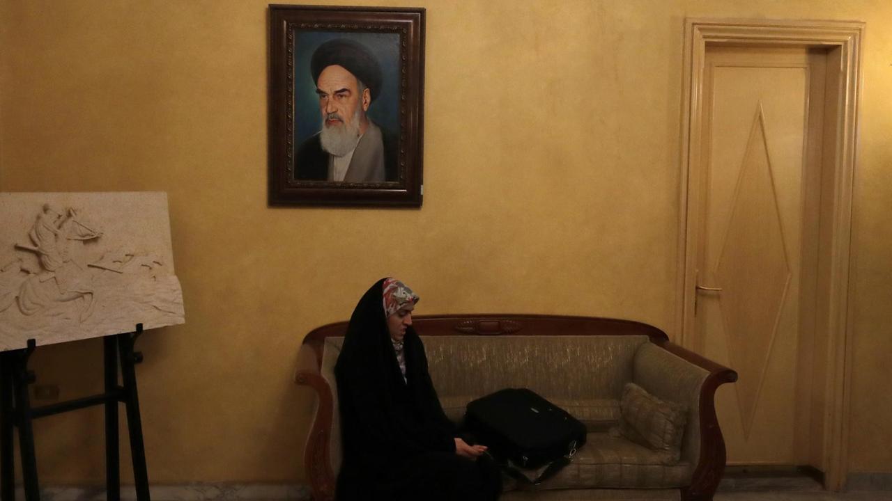 Eine iranische Staatsangestellte hört in der iranischen Botschaft im Libanon einer Pressekonferenz zu. Über ihr hängt ein Bild von Ayatollah Khomeini.