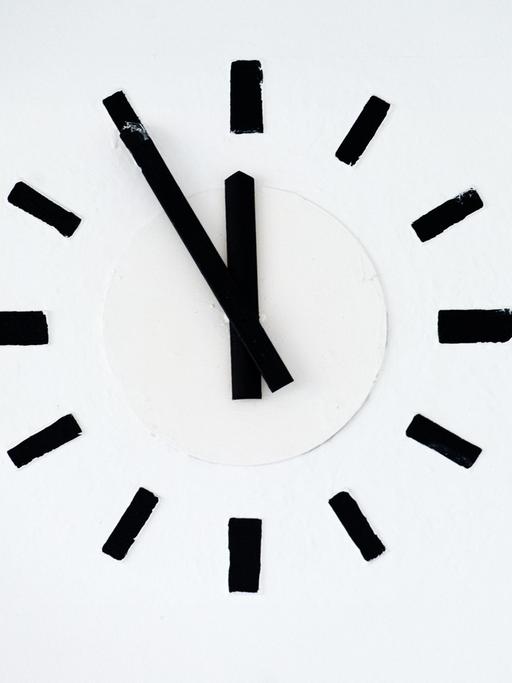 Eine Uhr zeigt fünf vor zwölf.