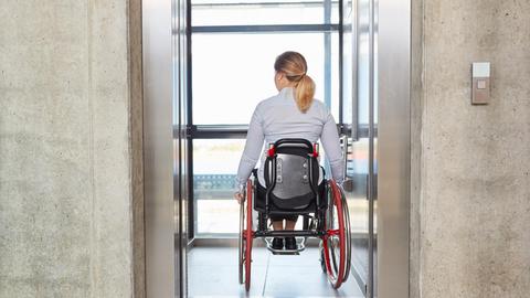 Eine Frau im Roll-Stuhl fährt mit dem Fahr-Stuhl in einem Gebäude 