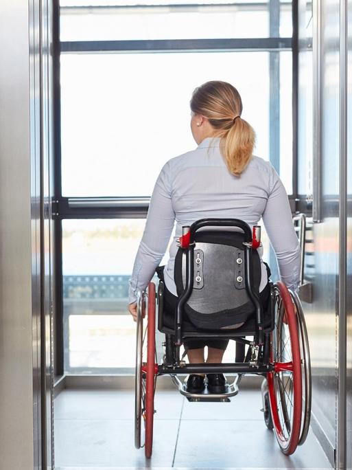 Eine Geschäftsfrau im Rollstuhl fährt mit dem Fahrstuhl in einem Geschäftsgebäude.