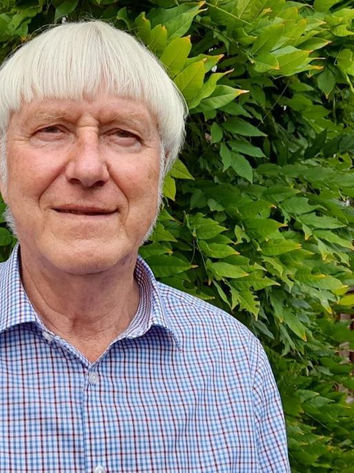 Ein Mann mit kurzen grauen Haaren steht in einem Garten.