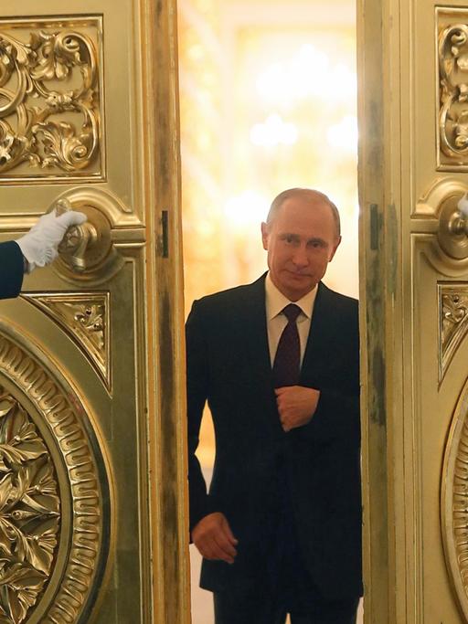 Wladimir Putin schreitet durch eine goldene Flügeltür, die ihm zwei Uniformiert öffnen