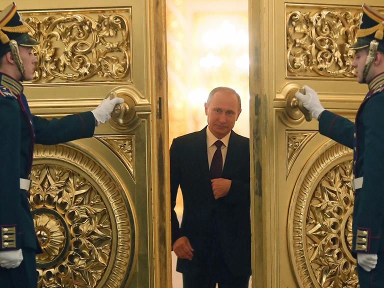 Wladimir Putin schreitet durch eine goldene Flügeltür, die ihm zwei Uniformiert öffnen