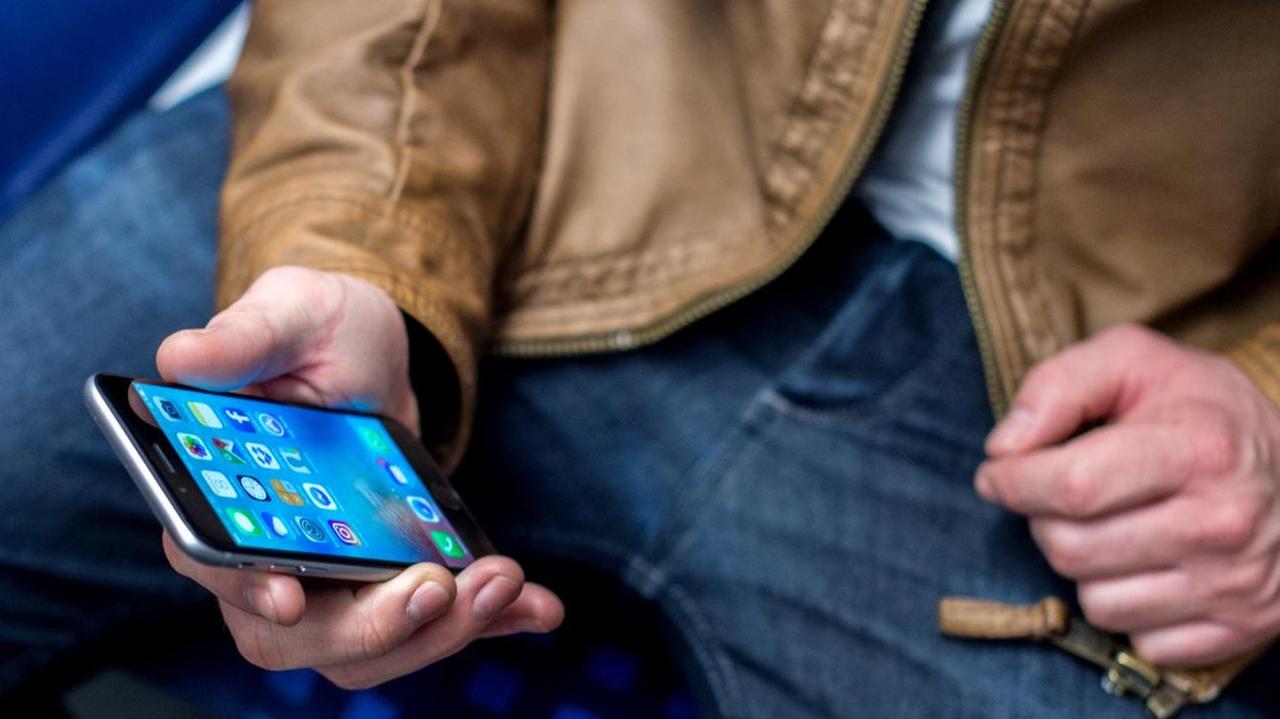 Ein junger Mann sitzt am 03.03.2017 in Frankfurt am Main (Hessen) in einer S-Bahn und benutzt dabei sein Smartphone.