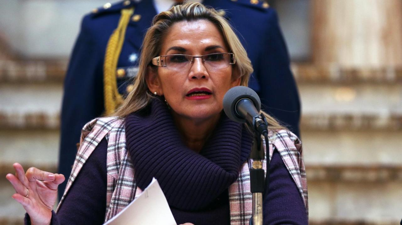 Die bolivianische Übergangspräsidentin Jeanine Áñez am 21. November im Palacio de Gobierno, dem bolivianischen Regierungssitz in La Paz. Eine Frau mit langen blonden Haaren und einer Brille sitzt vor einem Mikrofon und spricht.