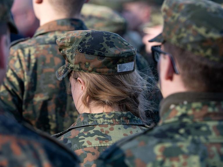 Soldaten stehen vor dem Tor zur Kaserne, im Mittelpunkt eine Soldatin