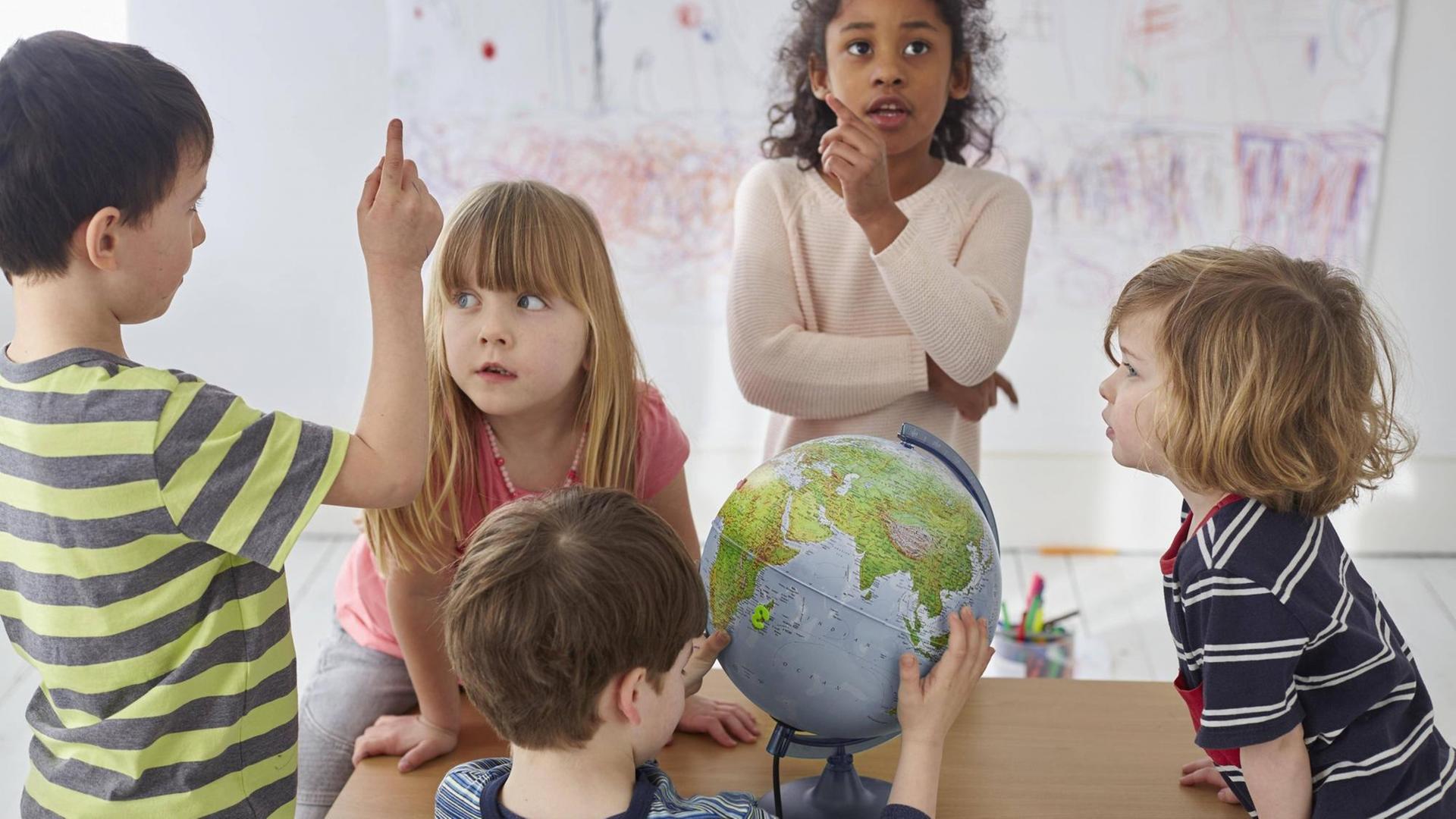 Diskutierende Kinder um einen Tisch, mit einem Globus.