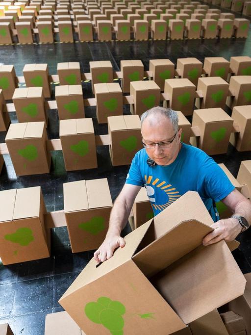 Ein Helfer steckt in der Dortmunder Messehalle einen der 25.000 Papphocker für den Evangelischen Kirchentag zusammen