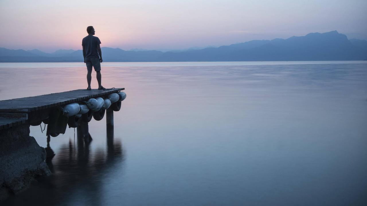 Ein Mann steht auf einem Steg am Gardasee.