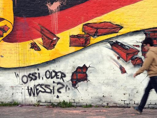 Ein Passant geht an einem Wandbild mit der deutschen Nationalflagge und dem Schriftzug "Ossi oder Wessi?" vorbei.