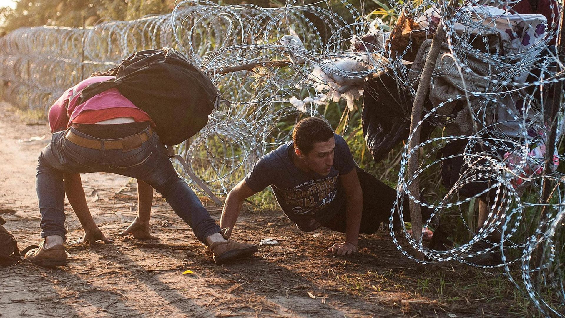 Migranten drängen sich durch einen Stachdeldrahtzaun.