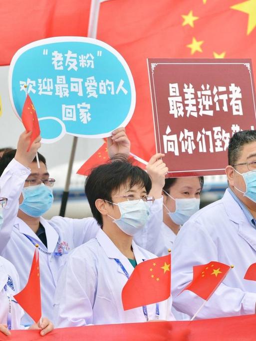Krankenhausmitarbeiter in der chinesischen Stadt Nanning, mit Kittel und Mundschutz bekleidet, halten Schilder und chinesische Flaggen hoch.
