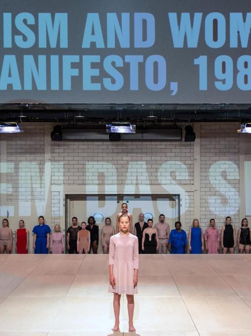 Eine Frau steht auf einer Theaterbühne, im Hintergrund stehen die Wörter: "Facism and Woman Manifesto, 1986" und "Jedem das seine"