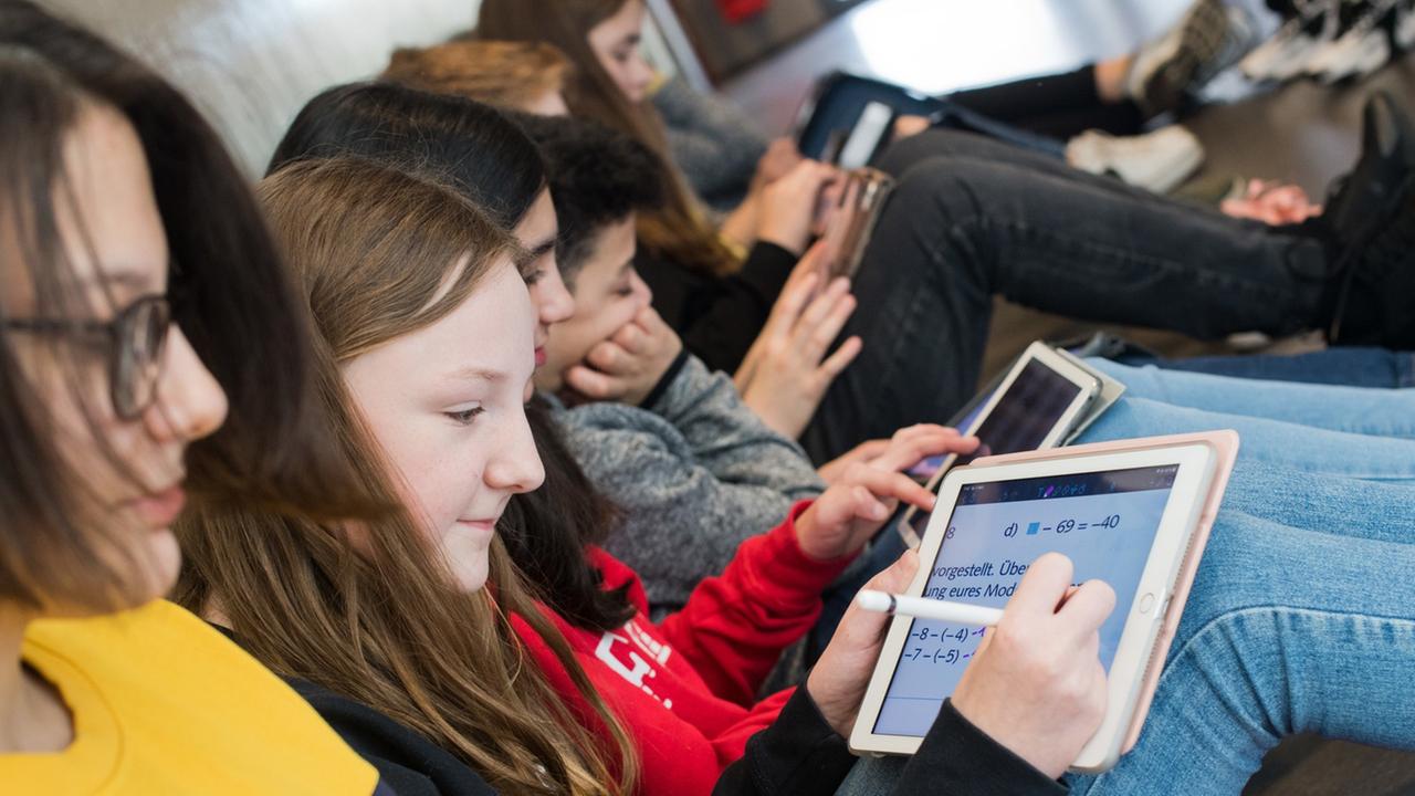 Schüler einer 7. Klasse sitzen auf dem Boden und lernen mit iPads im Matheunterricht an der Oberschule Gehrden in der Region Hannover.
