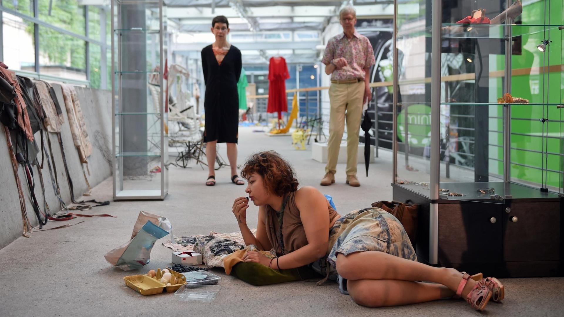 Eine Frau liegt in Berlin im Rahmen der 9. Berlin Biennale in der Akademie der Künste in Berlin bei einer Live-Installation auf dem Boden und isst.