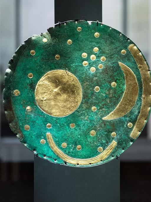 Eine antike grüne Scheibe mit Sternsymbolen steht in einer Vitrine.