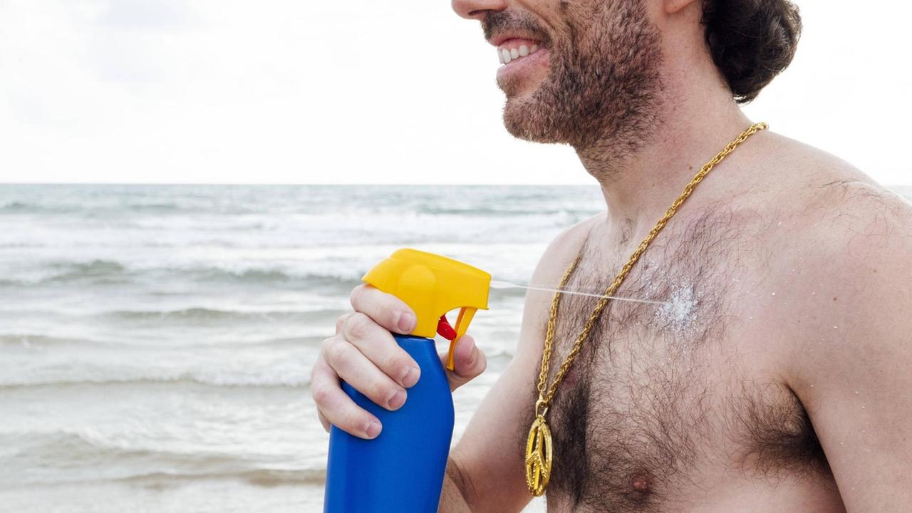 Ein Mann besprüht sich mit Sonnencreme am Strand.