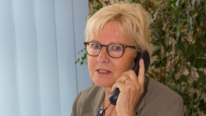 Christine Burck. Eine Frau mit Brille und kurzen blonden Haaren sitzt an einem Schreibtisch in einem Büro und telefoniert.