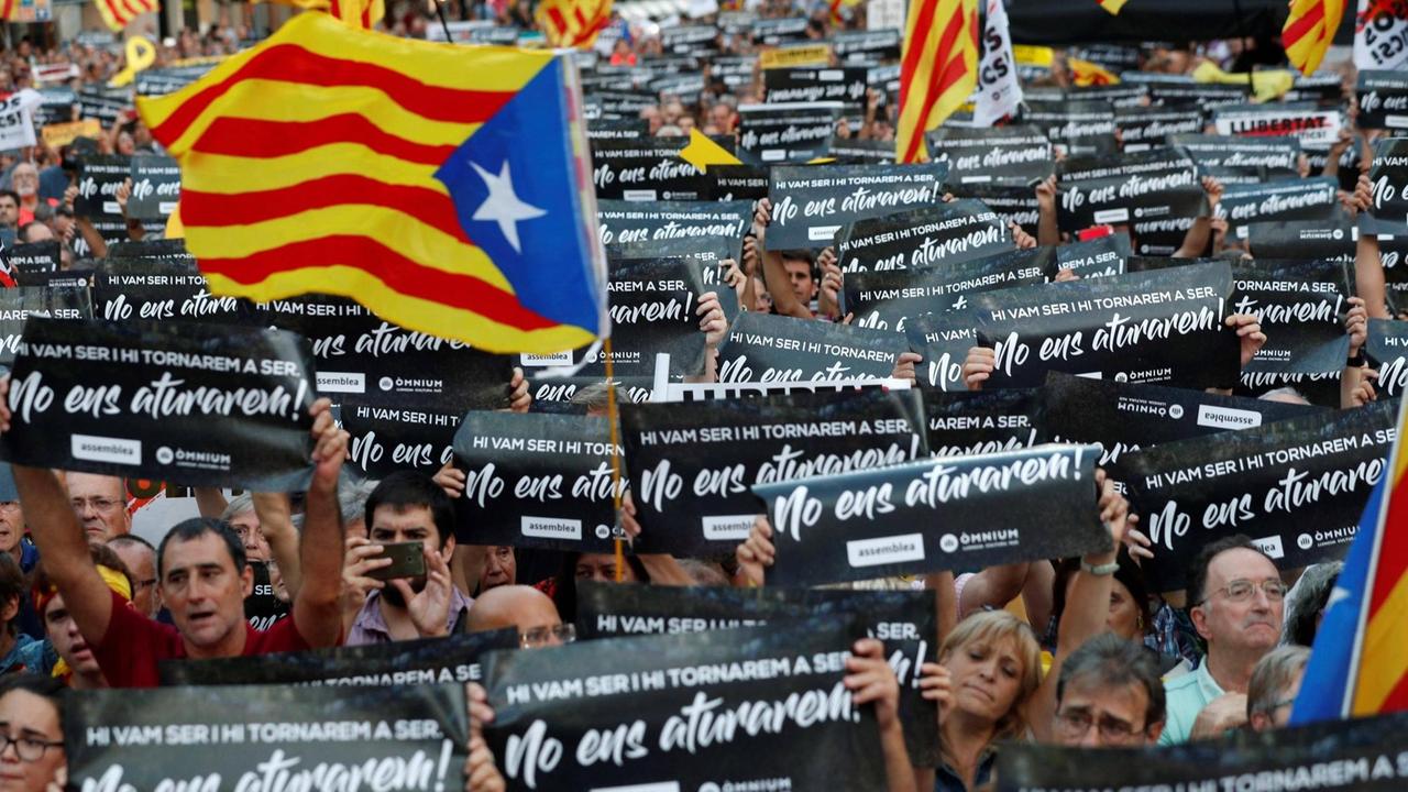 Sie sehen viele Menschen auf der Kundgebung, sie halten Plakate in die Luft schwenken und die katalanische Flagge.