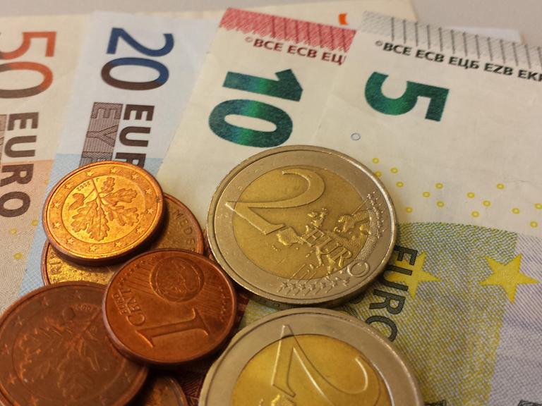 Euro-Geldscheine liegen mit Euro-Münzen auf einem Stapel.