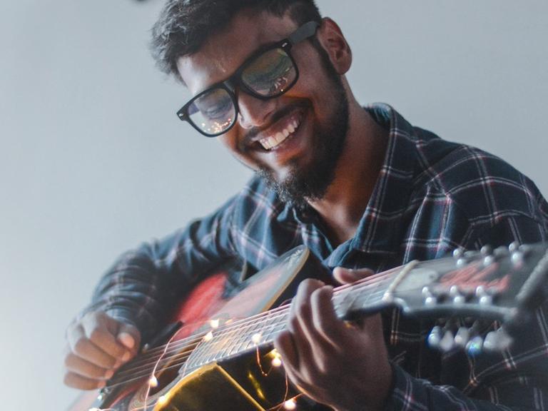Ein junger Mann lacht glücklich während er Gitarre spielt.