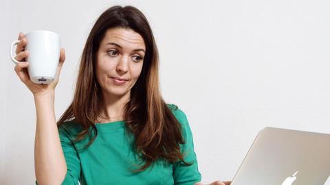 Eine junge Frau sitzt an einem Laptop und schaut skeptisch auf den Bildschirm